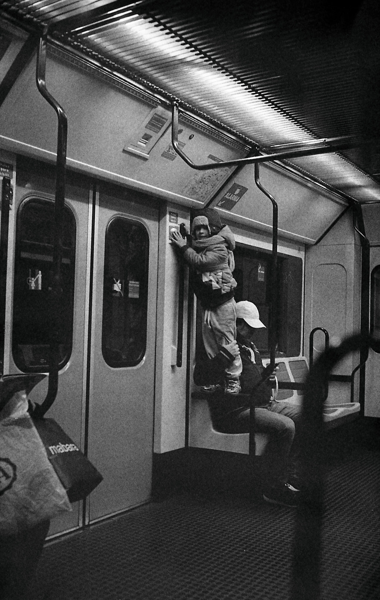 Black and white picture of kid standing on an armrest in the Madrid subway